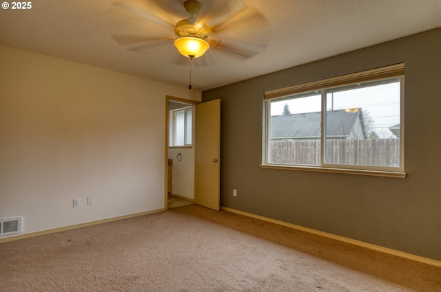 empty room featuring visible vents, a textured ceiling, carpet flooring, baseboards, and ceiling fan