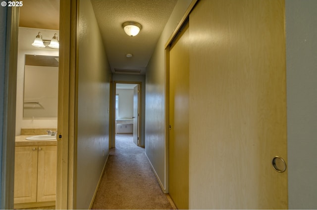 corridor with a sink, carpet flooring, baseboards, and a textured ceiling