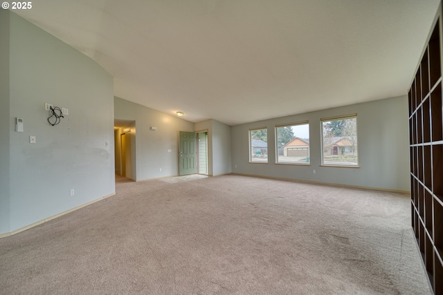 spare room featuring vaulted ceiling, light colored carpet, and baseboards