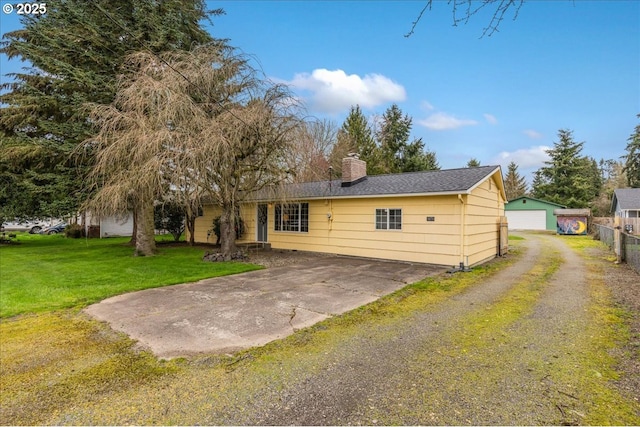 back of property with an outbuilding, driveway, a chimney, a detached garage, and a lawn