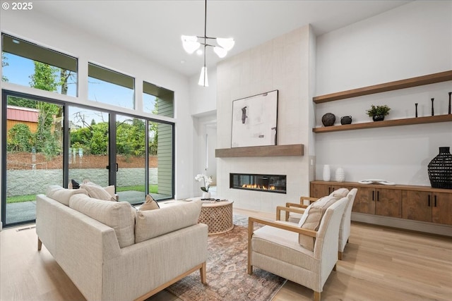 living room featuring a notable chandelier, a high ceiling, a tile fireplace, and light wood finished floors
