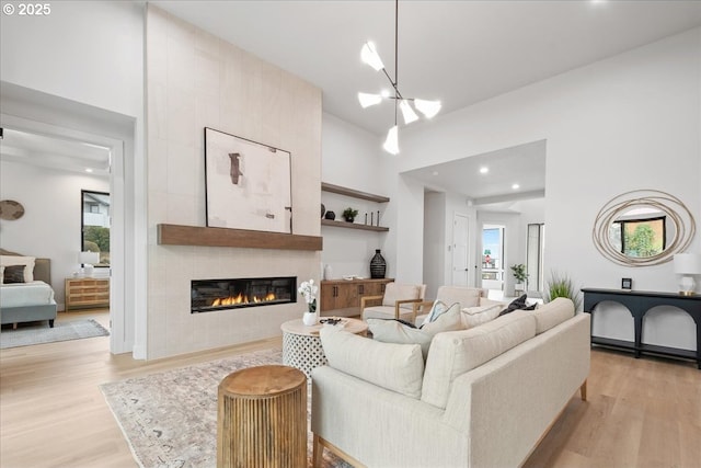 living room featuring light wood finished floors, a tile fireplace, a high ceiling, and a wealth of natural light