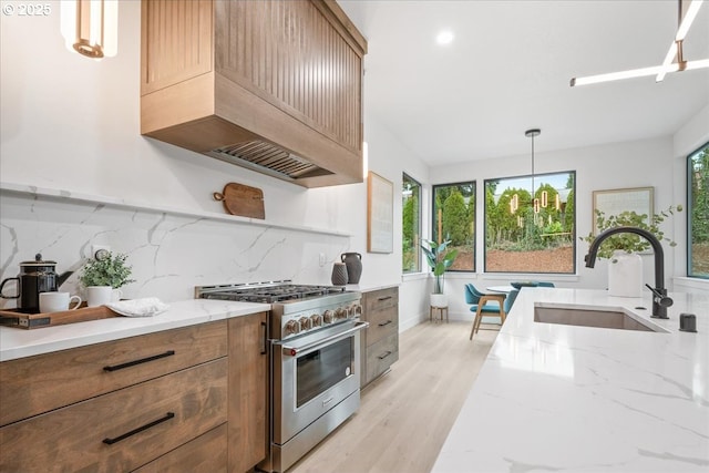 kitchen with premium range hood, light stone counters, light wood-style floors, stainless steel stove, and a sink