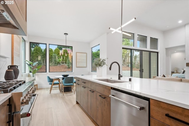 kitchen featuring light wood finished floors, light stone countertops, custom range hood, appliances with stainless steel finishes, and a sink