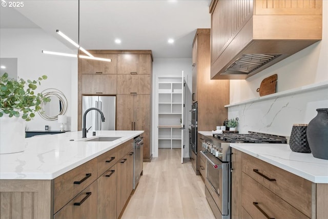 kitchen featuring light stone countertops, open shelves, a sink, custom range hood, and appliances with stainless steel finishes