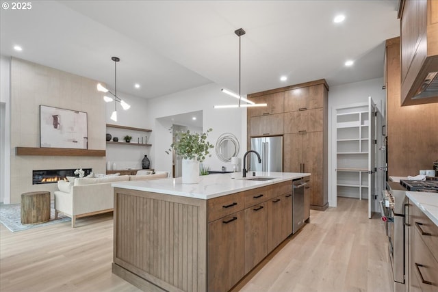 kitchen with light wood-type flooring, modern cabinets, an island with sink, a sink, and high end appliances
