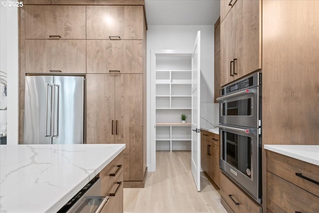 kitchen with light wood-type flooring, stainless steel appliances, modern cabinets, and light stone countertops
