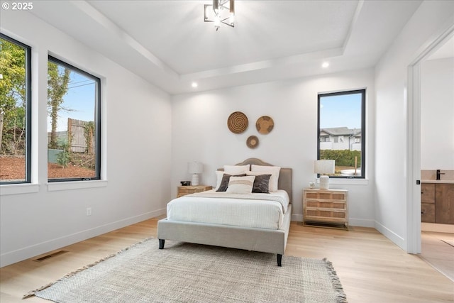 bedroom with a tray ceiling, multiple windows, and light wood-type flooring