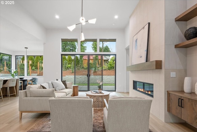 living area featuring a glass covered fireplace, light wood-style flooring, recessed lighting, and a high ceiling