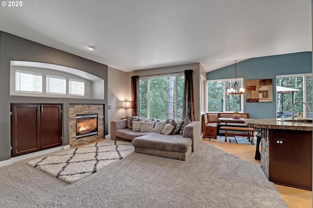 living room with sink, a stone fireplace, vaulted ceiling, and a chandelier