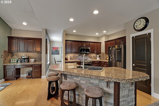 kitchen featuring a breakfast bar, sink, built in desk, a center island with sink, and stainless steel appliances