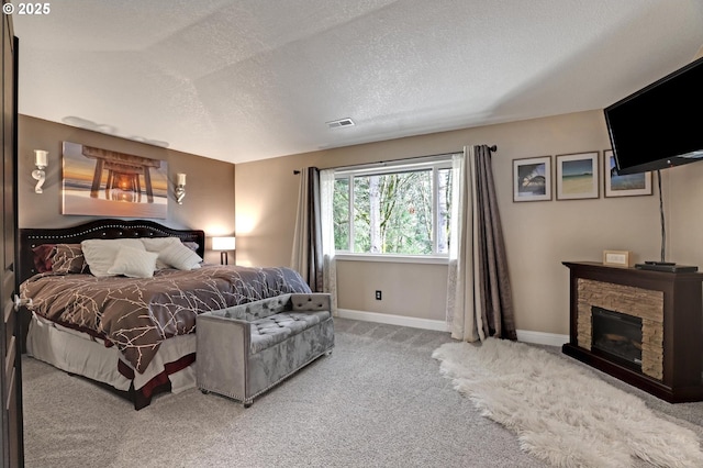 bedroom with a stone fireplace, carpet floors, and a textured ceiling