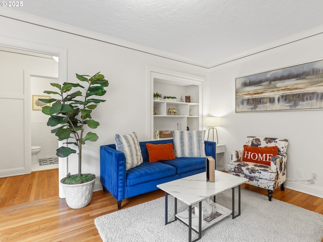 living room featuring visible vents, baseboards, built in features, wood finished floors, and a textured ceiling