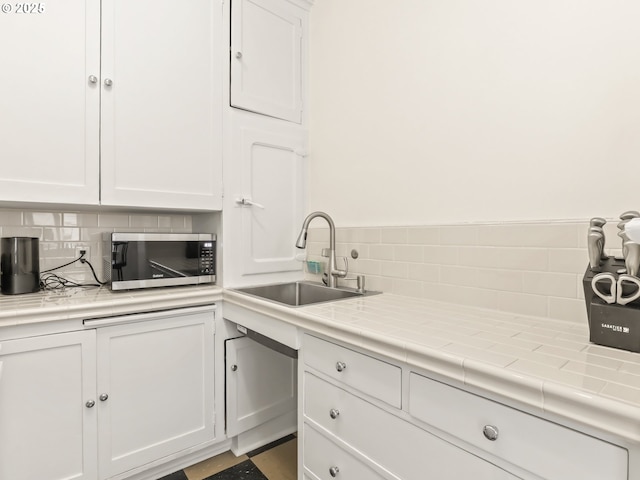 kitchen featuring backsplash, stainless steel microwave, white cabinets, and a sink