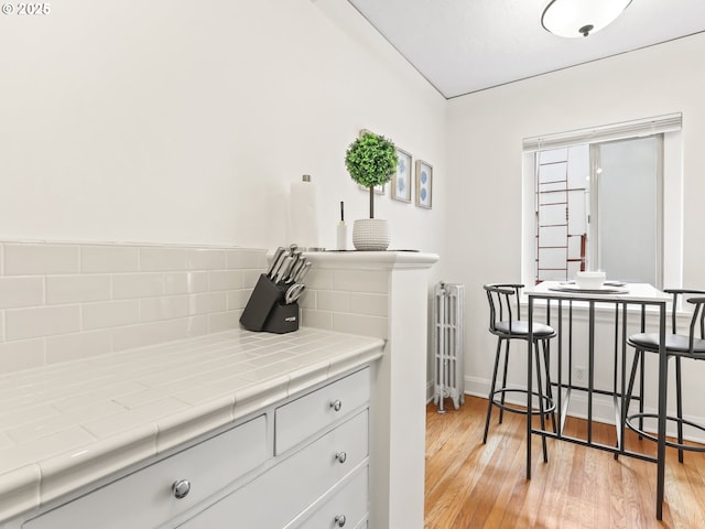 kitchen with tile countertops, radiator, white cabinets, and light wood finished floors