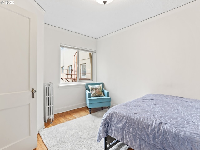 bedroom featuring radiator heating unit, wood finished floors, and baseboards