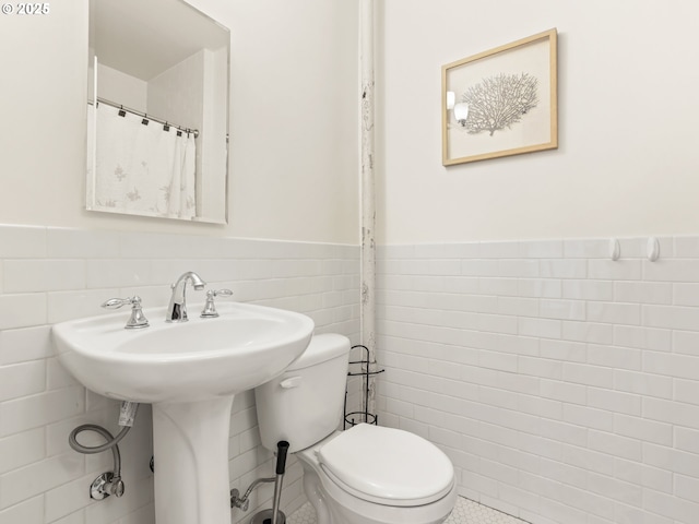 full bathroom featuring a wainscoted wall, toilet, and tile walls