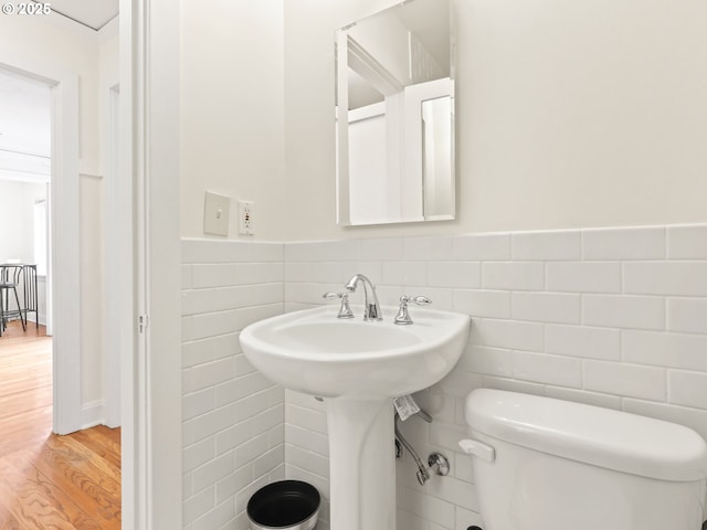 half bathroom featuring toilet, tile walls, wood finished floors, and wainscoting