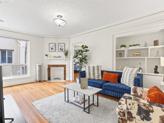 living area with radiator, wood finished floors, a fireplace with flush hearth, and a textured ceiling