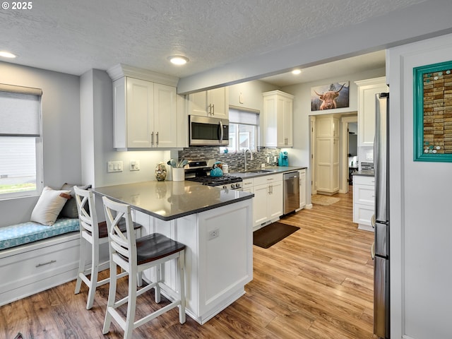 kitchen with a breakfast bar, sink, light hardwood / wood-style floors, kitchen peninsula, and stainless steel appliances