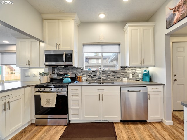 kitchen with stainless steel appliances, sink, light hardwood / wood-style floors, and decorative backsplash