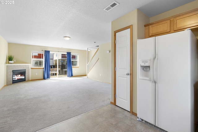 interior space featuring light colored carpet, a tiled fireplace, white fridge with ice dispenser, stairs, and visible vents