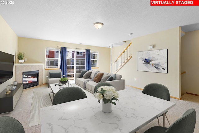 dining space with a tiled fireplace, stairs, baseboards, and light carpet