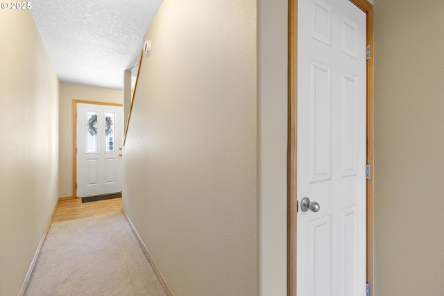 hall with a textured ceiling, baseboards, and light carpet