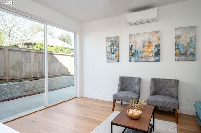 living area featuring light wood-type flooring, an AC wall unit, and baseboards