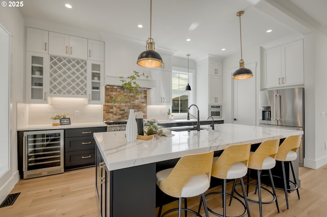 kitchen with beverage cooler, stainless steel appliances, a sink, light wood-type flooring, and recessed lighting