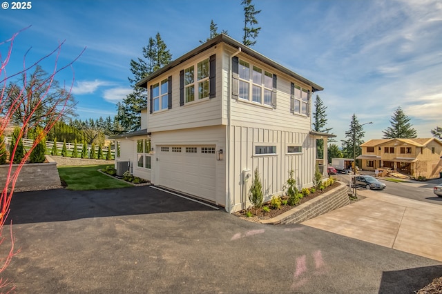view of home's exterior featuring board and batten siding, central AC unit, asphalt driveway, and an attached garage
