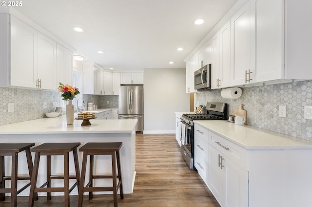 kitchen featuring a breakfast bar, wood finished floors, appliances with stainless steel finishes, a peninsula, and white cabinets