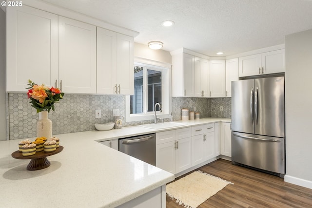 kitchen with a sink, backsplash, dark wood finished floors, white cabinetry, and appliances with stainless steel finishes