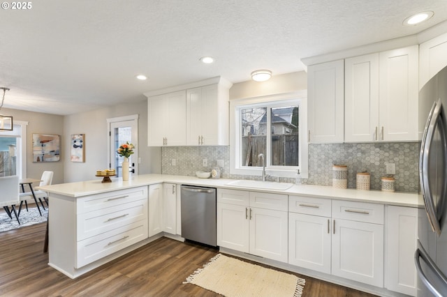 kitchen with a peninsula, dark wood-style floors, white cabinets, stainless steel appliances, and a sink