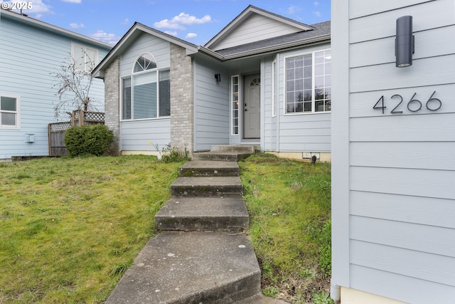 entrance to property with brick siding and a yard