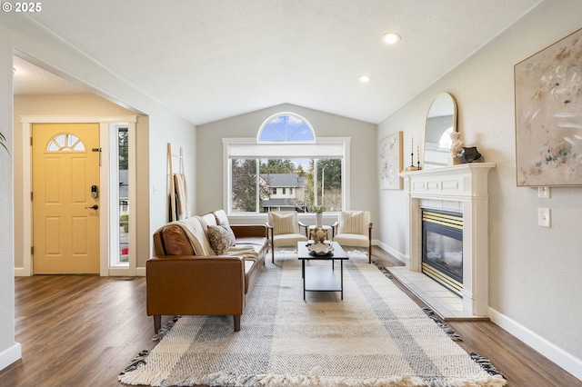 living area with a glass covered fireplace, vaulted ceiling, wood finished floors, and baseboards