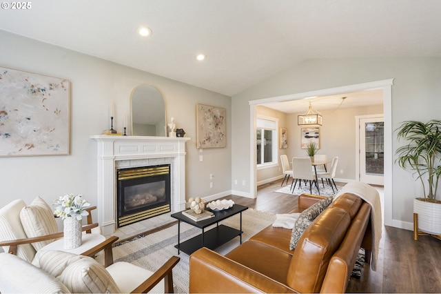 living area with baseboards, wood finished floors, a tiled fireplace, and vaulted ceiling