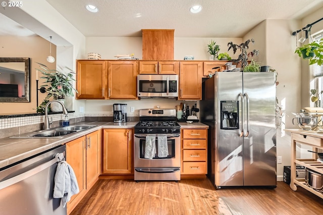 kitchen featuring light wood-type flooring, appliances with stainless steel finishes, brown cabinets, and a sink