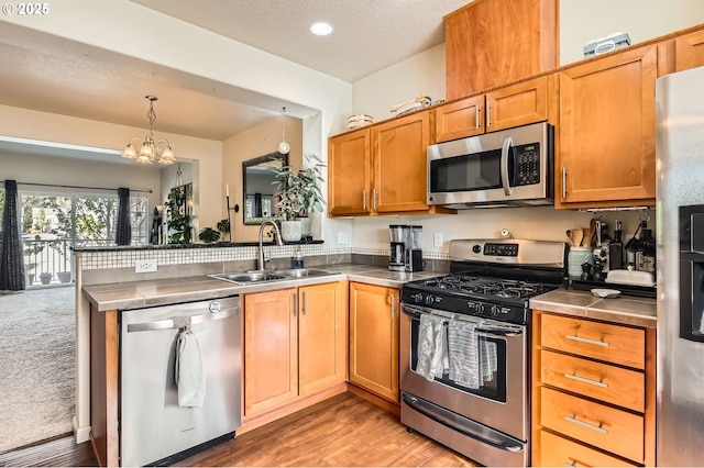 kitchen featuring a notable chandelier, a sink, a peninsula, light wood-style floors, and appliances with stainless steel finishes