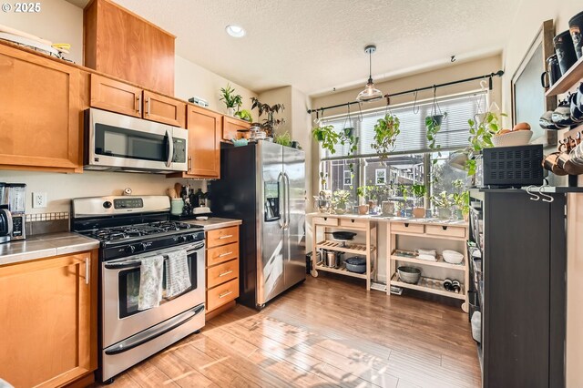kitchen featuring light wood-style flooring, a textured ceiling, tile countertops, appliances with stainless steel finishes, and recessed lighting