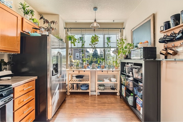 kitchen with brown cabinets, wood finished floors, a textured ceiling, tile countertops, and appliances with stainless steel finishes