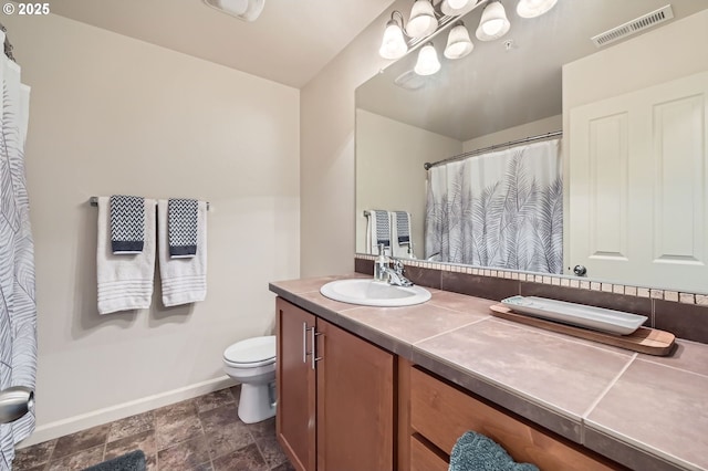 bathroom with toilet, stone finish flooring, visible vents, baseboards, and vanity