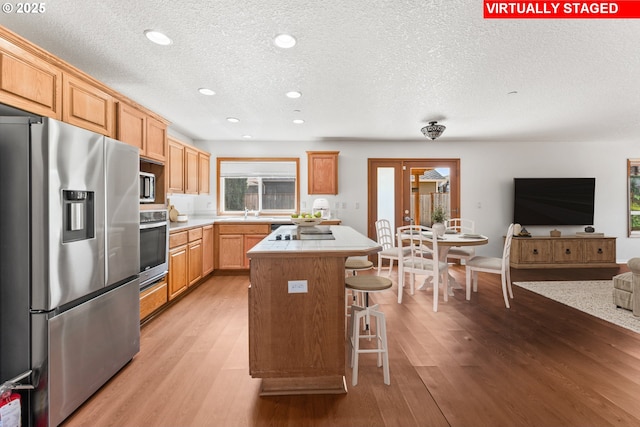 kitchen with stainless steel appliances, a textured ceiling, a center island, light countertops, and a breakfast bar area