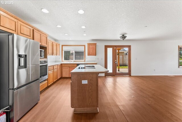 kitchen featuring stainless steel appliances, a kitchen island, a textured ceiling, light wood finished floors, and light countertops