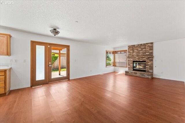 unfurnished living room featuring light wood-style floors, a textured ceiling, baseboards, and a fireplace