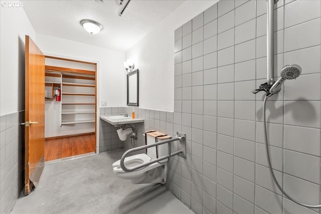 full bathroom with tile walls, a textured ceiling, toilet, a sink, and a wainscoted wall