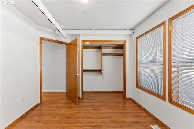 unfurnished bedroom featuring light wood-style floors, a closet, baseboards, multiple windows, and a textured ceiling