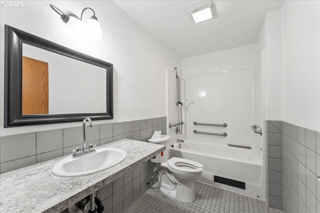 full bathroom featuring tile walls, a sink, tile patterned floors, toilet, and bathtub / shower combination