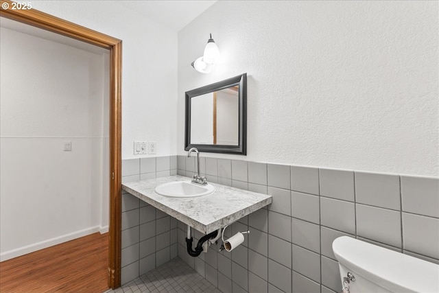 half bath with a sink, toilet, wood finished floors, and tile walls