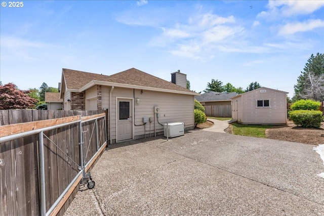 back of house with fence, a chimney, a patio, an outdoor structure, and a shingled roof